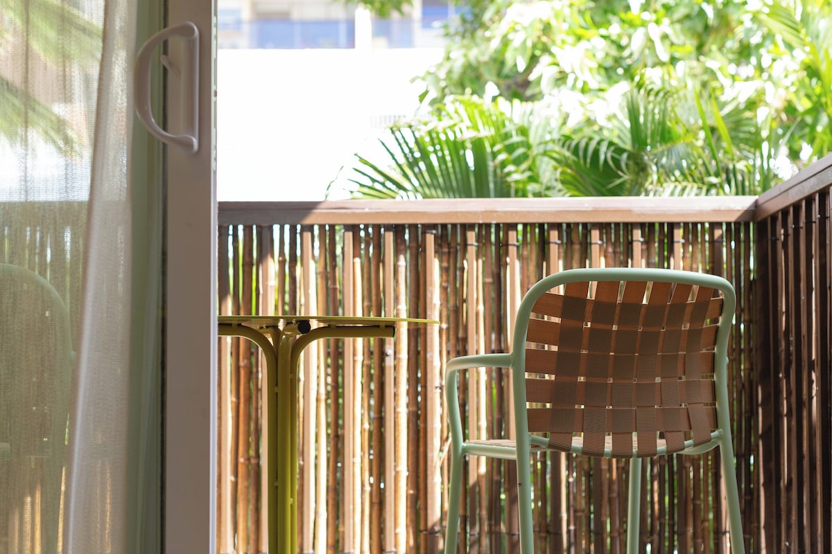Una valla de bambú, una silla verde y una mesa con estructura metálica.