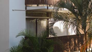 A multi-story building with balconies, large windows, and surrounding tropical plants.