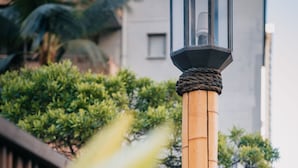 Una farola con una cuerda enrollada en su base, sobre un fondo de valla de madera y follaje.