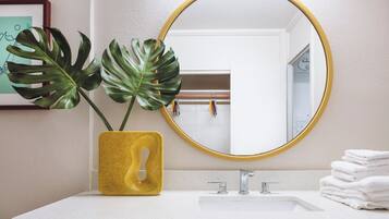 A bathroom with a white sink, a yellow vase with a plant, and a round mirror with a gold frame.