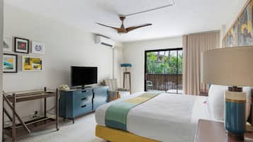 Habitación de hotel con cama, escritorio con teléfono, televisión y balcón con vista a follaje.