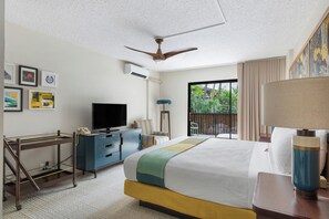 A hotel room with a bed, a desk with a telephone, a television, and a balcony with a view of greenery. - White Sands Hotel (Honolulu)