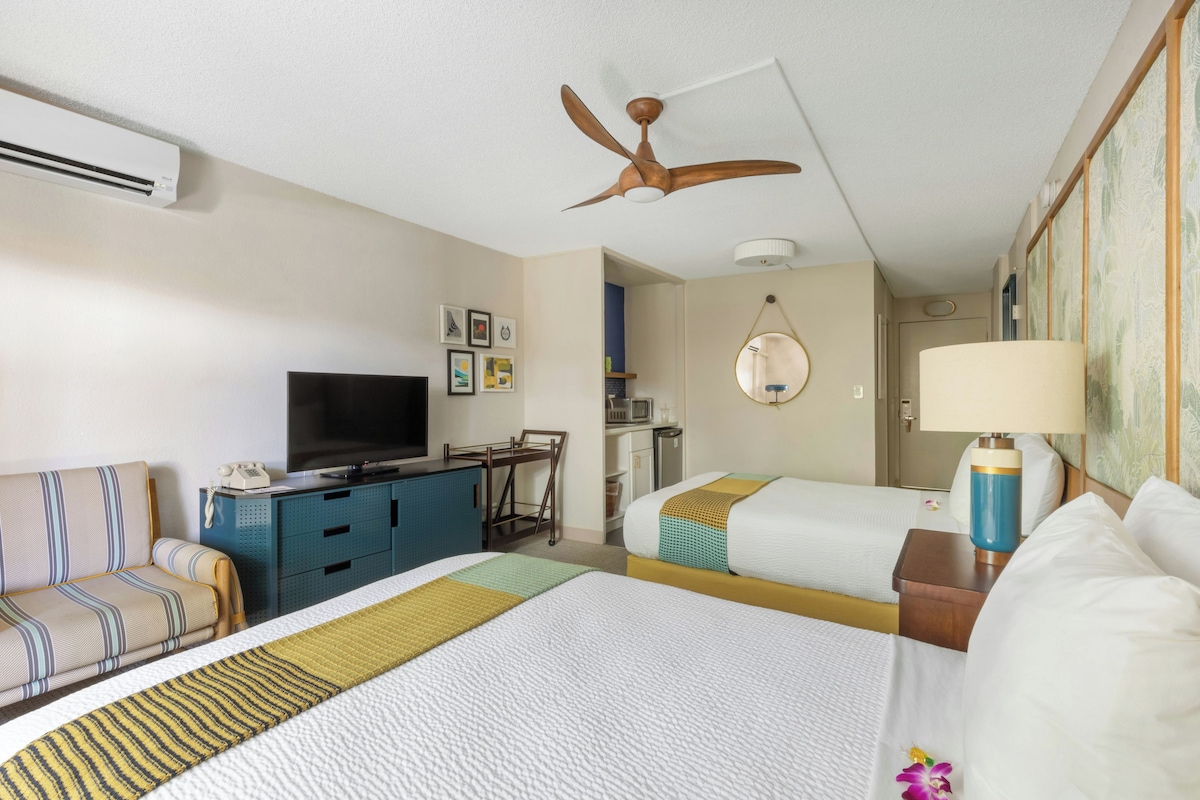 Habitación de hotel con cama, sofá, escritorio, televisor y ventilador de techo.