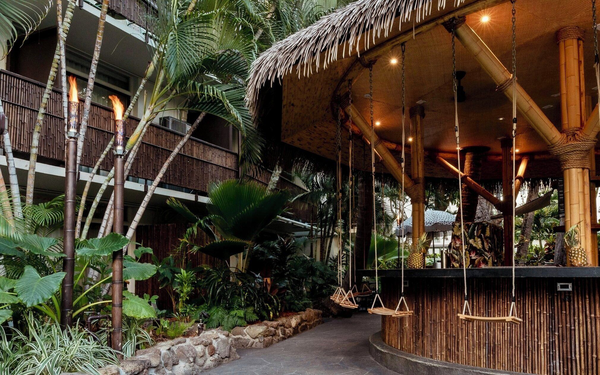 A tropical resort with a bamboo structure, hanging swings, and lush vegetation.