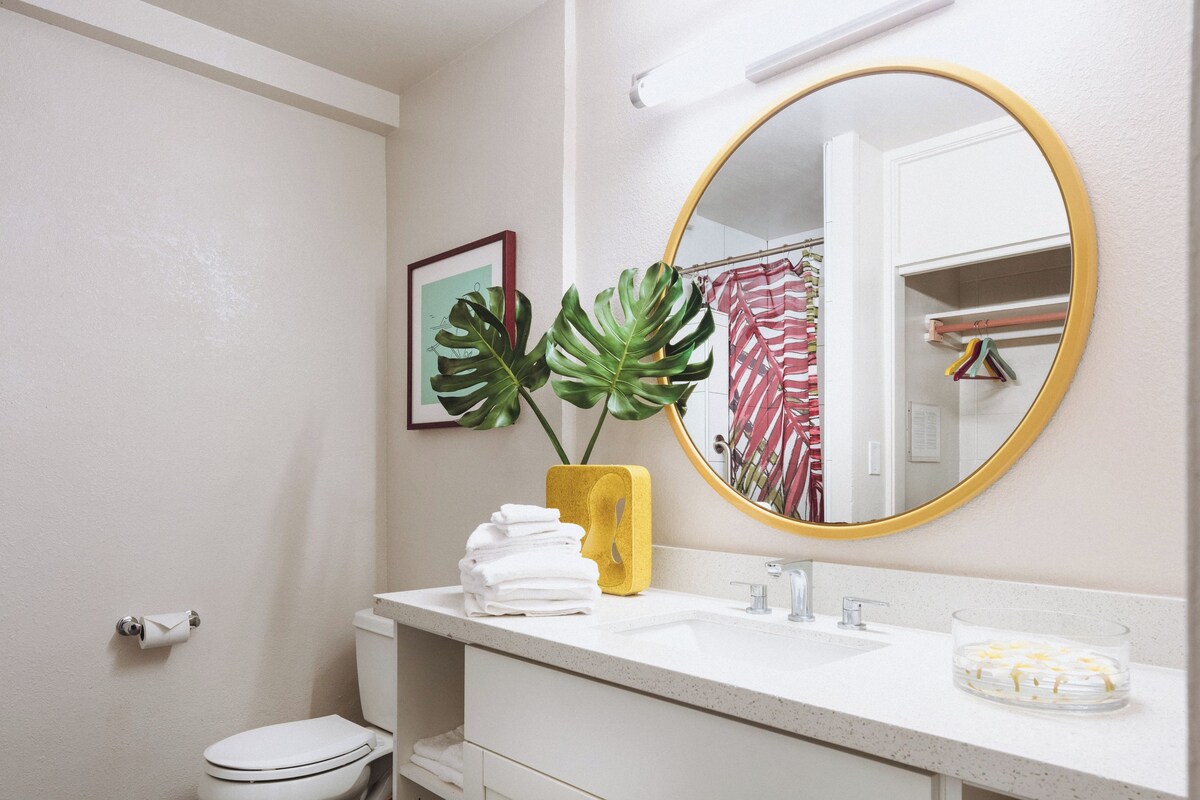 A bathroom with a toilet, sink, mirror, and a plant in a yellow vase.