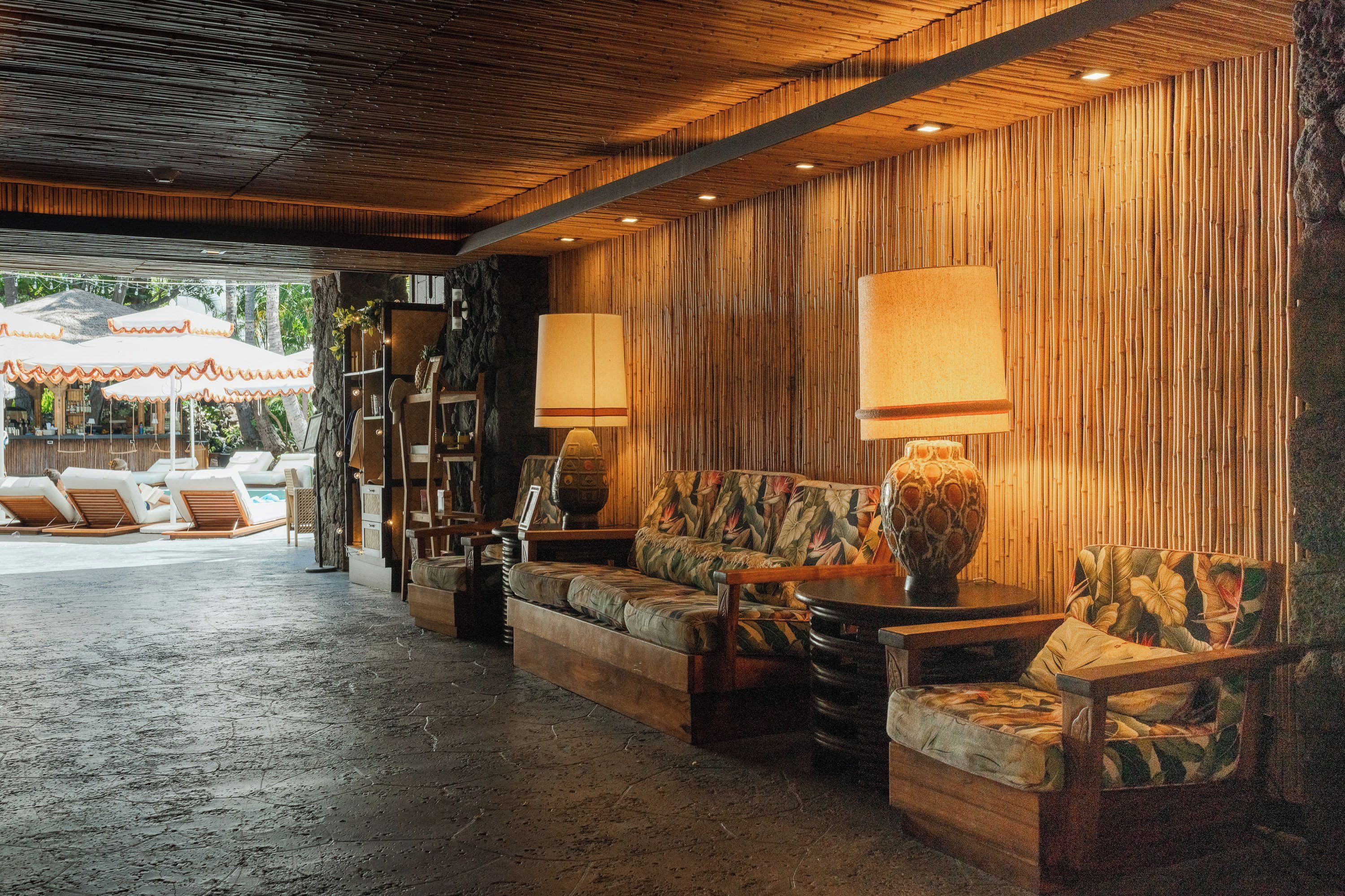 A lounge area with a sofa, armchairs, and a table, featuring a bamboo wall and a ceiling with wooden slats.