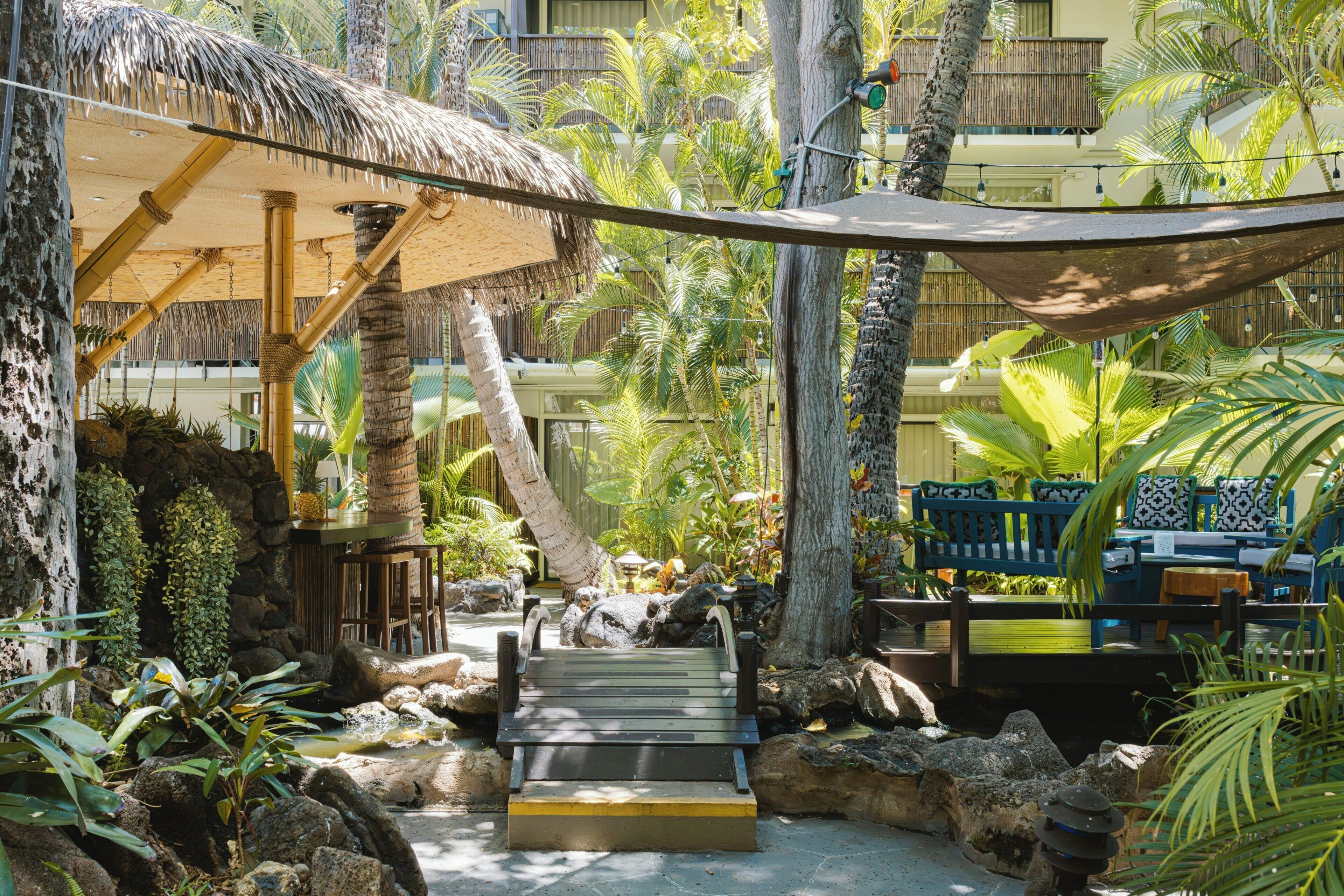A tropical resort with a thatched-roof structure, outdoor seating, and a water feature.