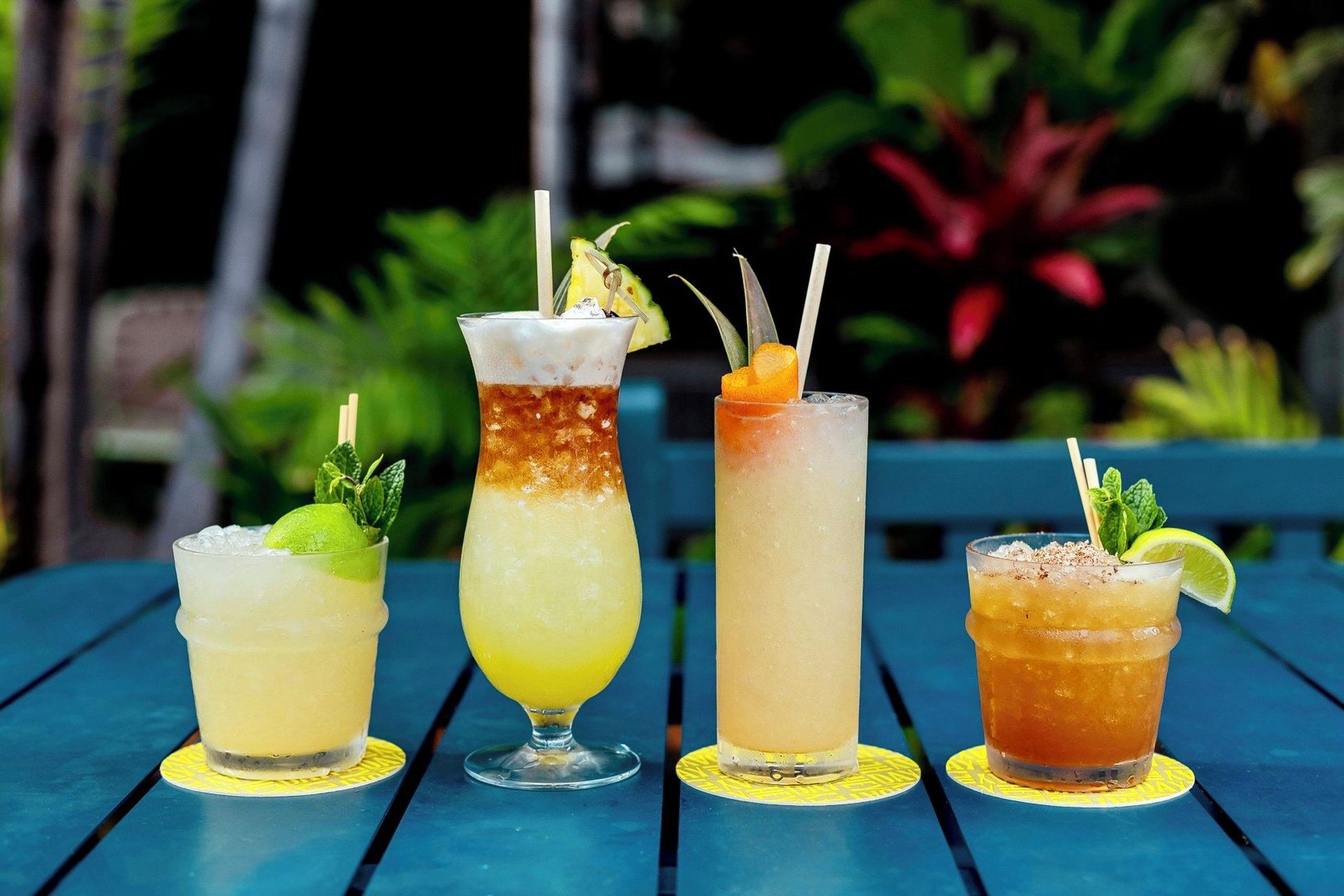 Four different cocktails on a blue table with a tropical background.