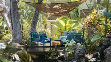 Un espace extérieur paisible, aménagé avec deux chaises bleues et une table, entouré d’une végétation tropicale luxuriante et agrémenté d’un petit élément décoratif aquatique.
