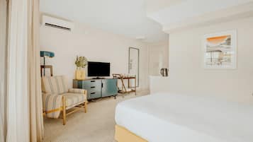 A hotel room with a bed, a TV, a desk, a chair, a plant, and a painting.