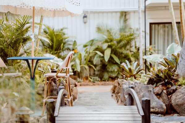 A wooden deck leading to a house with a white exterior, surrounded by tropical plants and a small table with chairs. - White Sands Hotel (Honolulu)