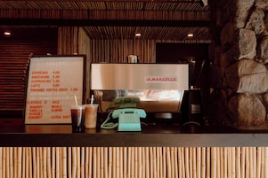 Eine Kaffeemaschine mit einer Speisekarte, die Kaffeesorten und Preise auflistet, ein Telefon und eine Steinwand.