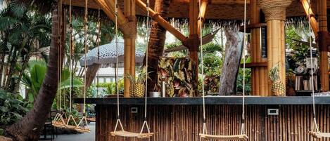 A tropical-themed bar area with bamboo columns, hanging swings, and a tropical mural.