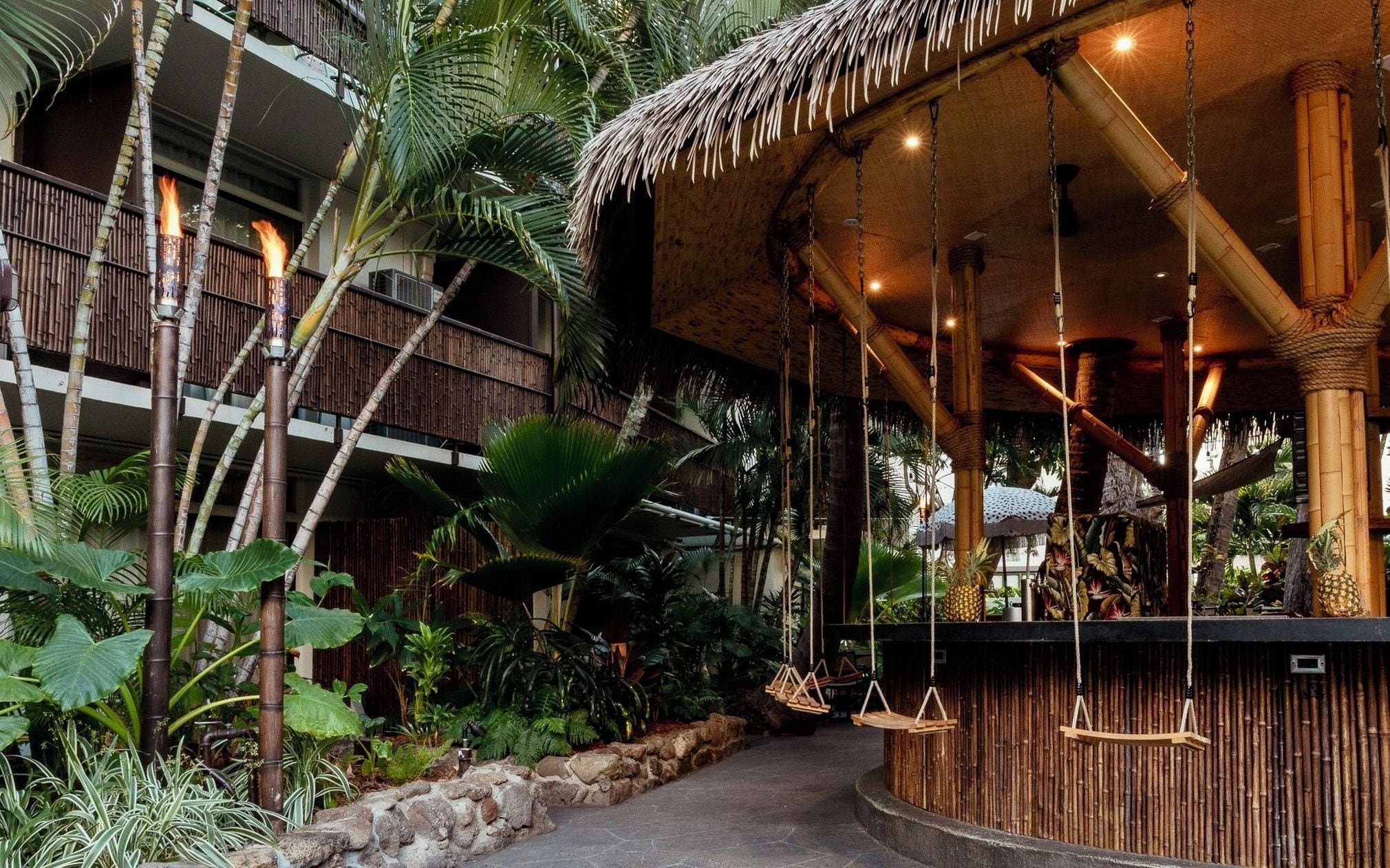 A tropical resort with a bamboo structure, hanging swings, and lush vegetation.
