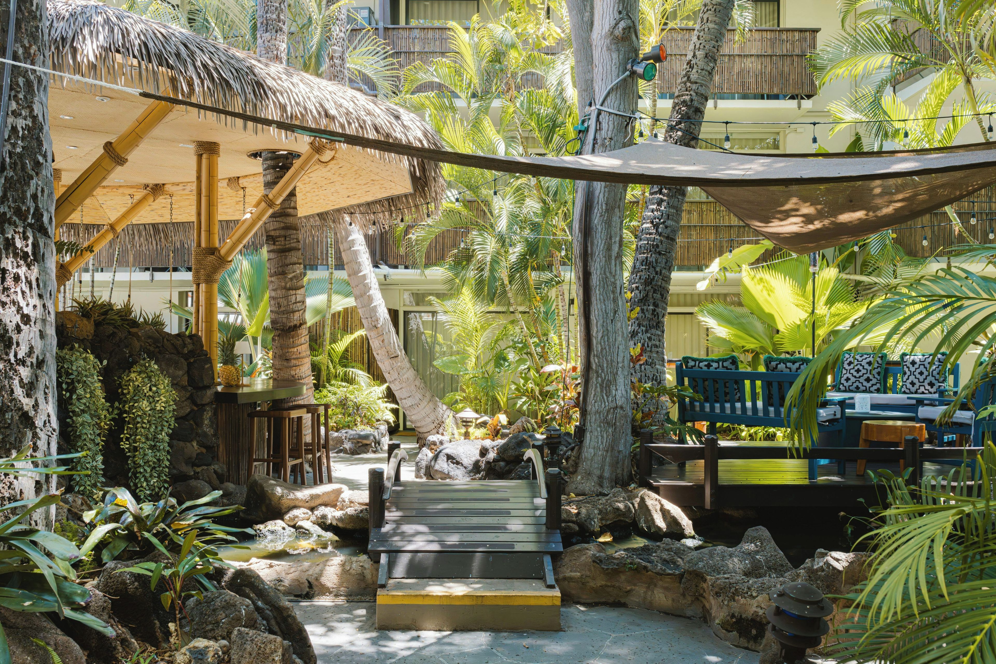 A tropical resort with a thatched-roof structure, outdoor seating, and a water feature.