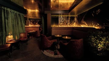 Ein schwach beleuchteter Lounge-Bereich mit Ledersitzgelegenheiten, einem gemusterten Teppich und einem an der Wand montierten Aquarium.
