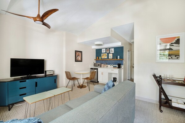 A modern living room with a flat-screen TV, a sofa, a dining table, and a kitchen area with a microwave and sink. - White Sands Hotel (Honolulu)