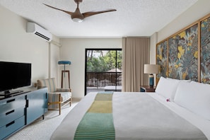 Habitación de hotel con cama, televisión, escritorio, silla, balcón con cortinas y ventilador de techo.