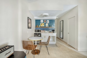 A compact kitchen with a microwave, refrigerator, and a small dining area with two wicker chairs and a white table.