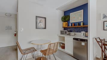 Una cucina compatta con forno a microonde, lavello e lavastoviglie, un tavolo da pranzo rotondo con due sedie e una parete decorata in blu.