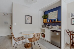 Cocina compacta con microondas, pileta y lavavajillas, una mesa de comedor redonda con dos sillas y una pared azul.