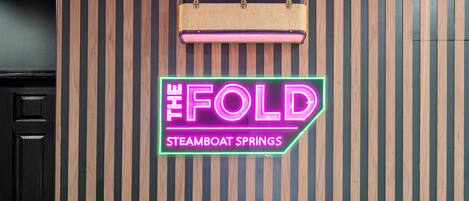 Ein Empfangsschalter mit einem Neonzeichen, auf dem "The Fold Steamboat Springs" steht, und einem alten Koffer darauf.