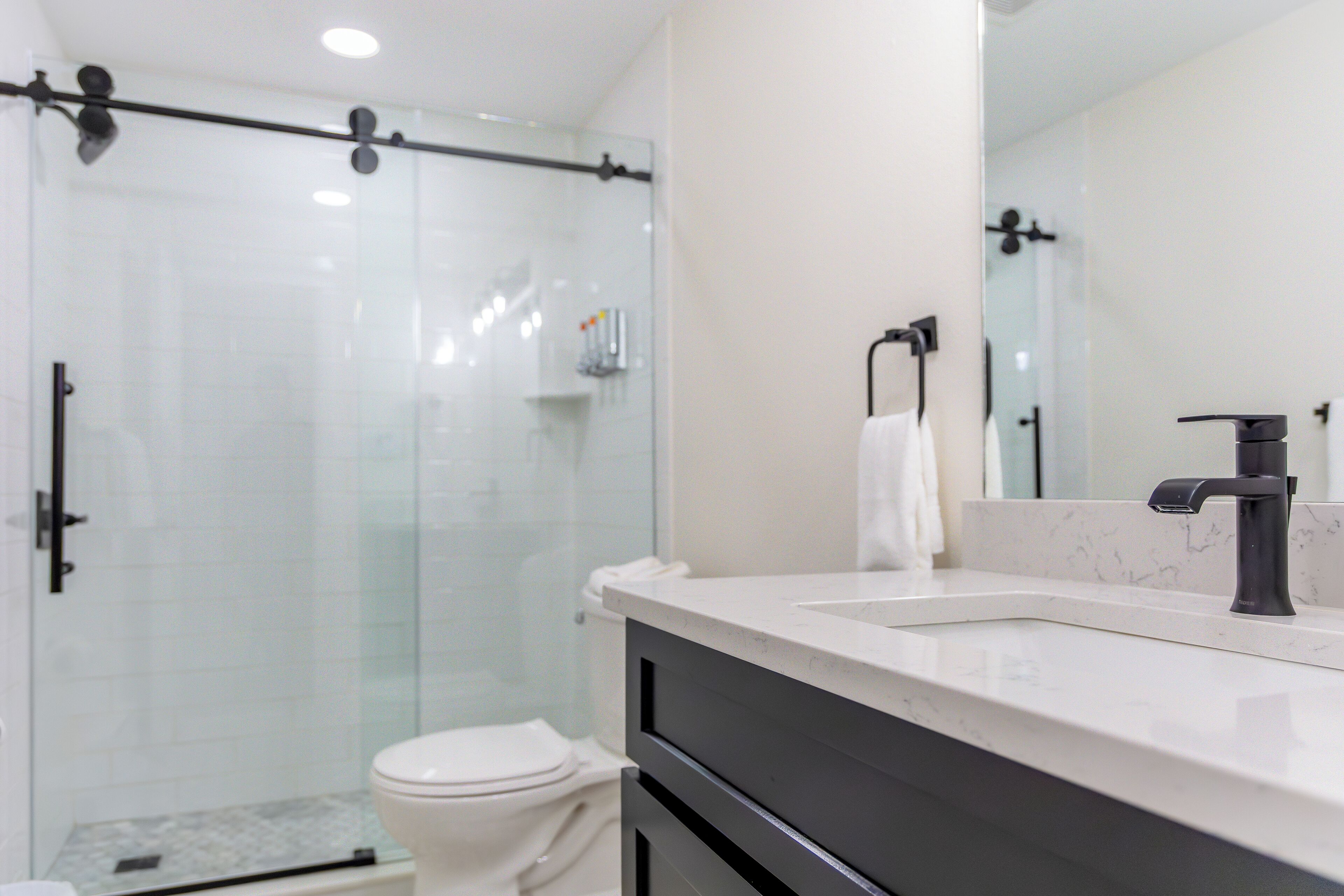 A modern bathroom with a glass shower enclosure, a white toilet, and a vanity with a black faucet.
