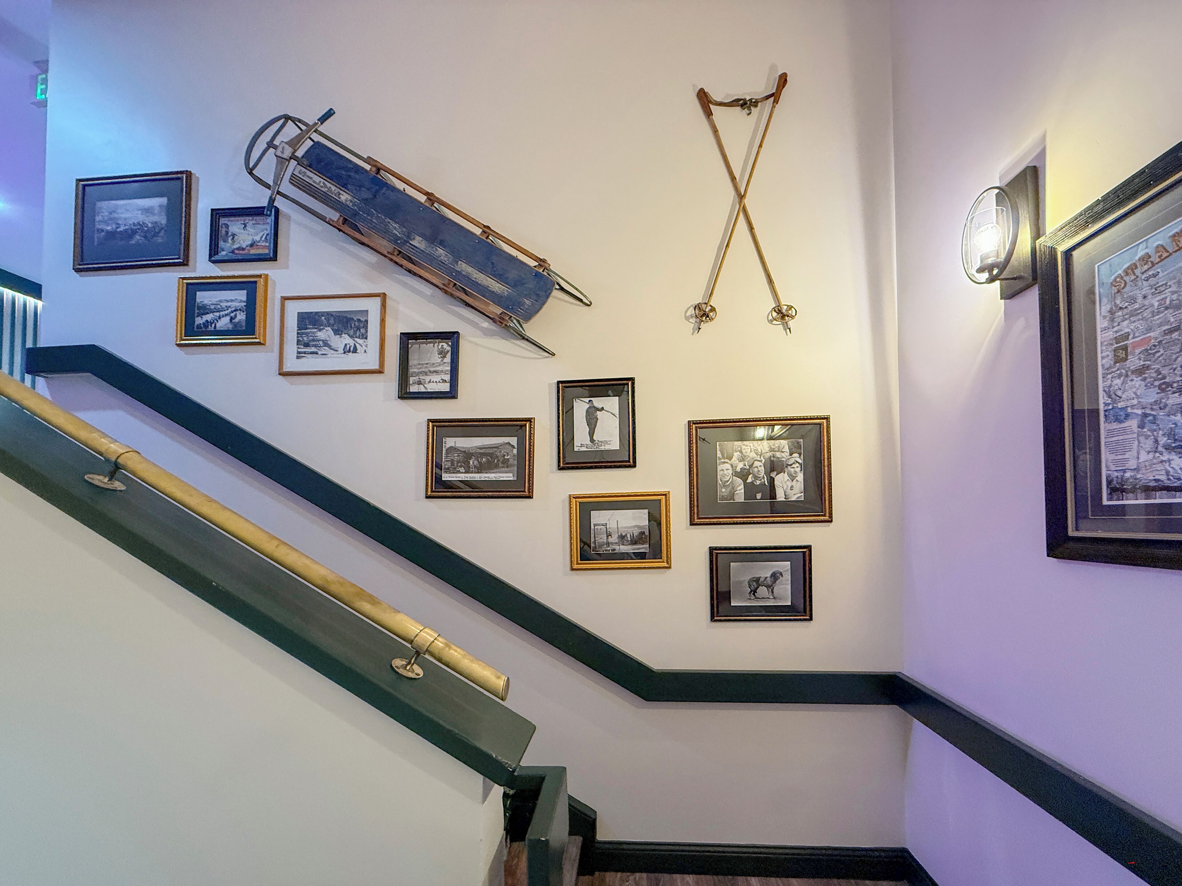 Una escalera con barandilla, una pared con fotografías enmarcadas y una lámpara de pared.