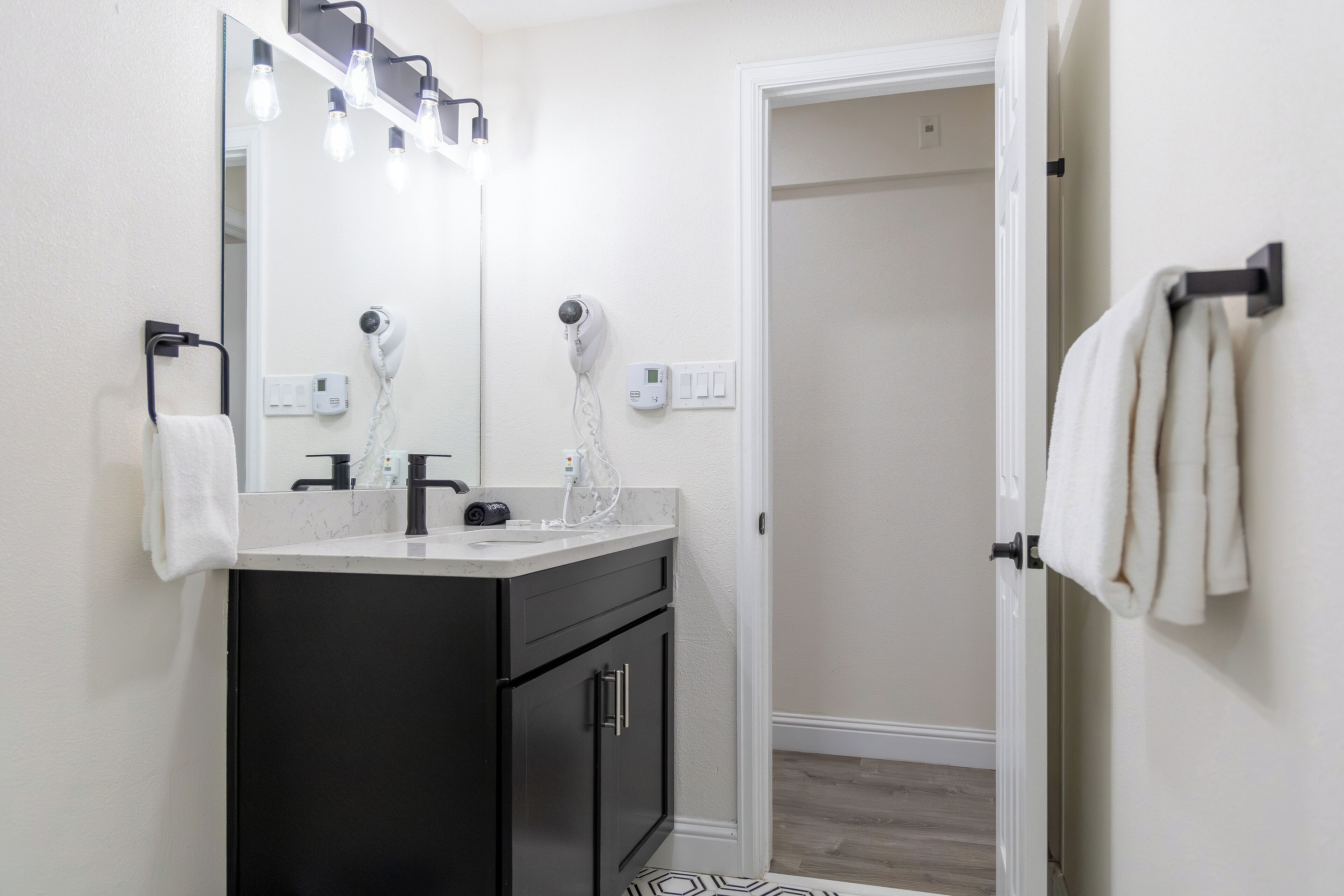A modern bathroom with a black vanity, a large mirror, and a hairdryer.