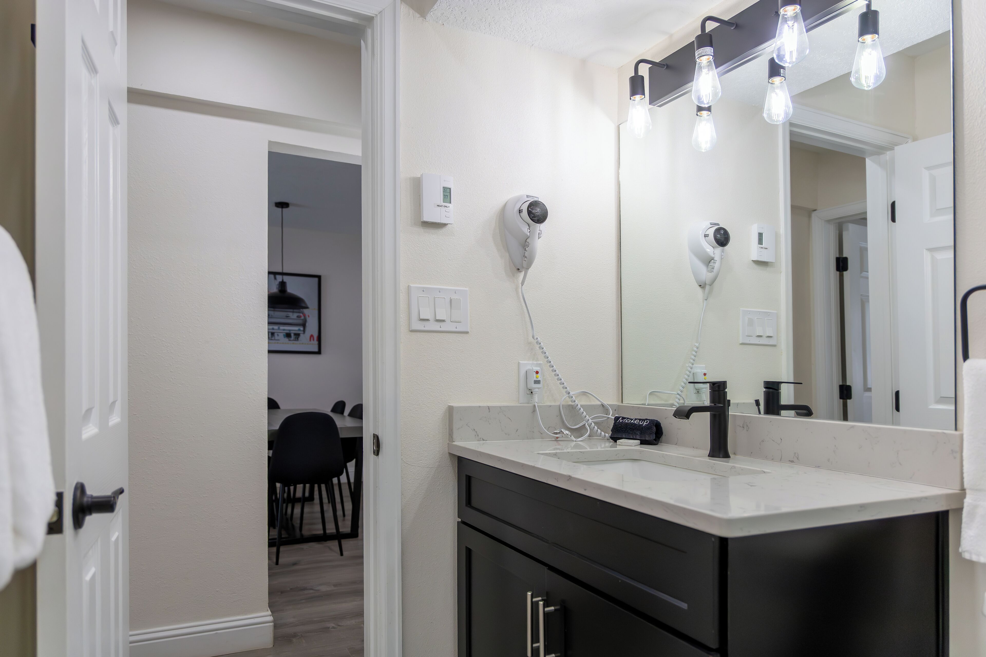 A bathroom with a white vanity, a large mirror, and a hairdryer mounted on the wall.