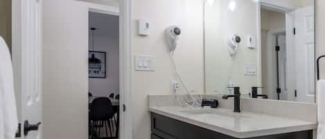 Un baño con tocador blanco, un espejo grande y un secador de pelo montado en la pared.
