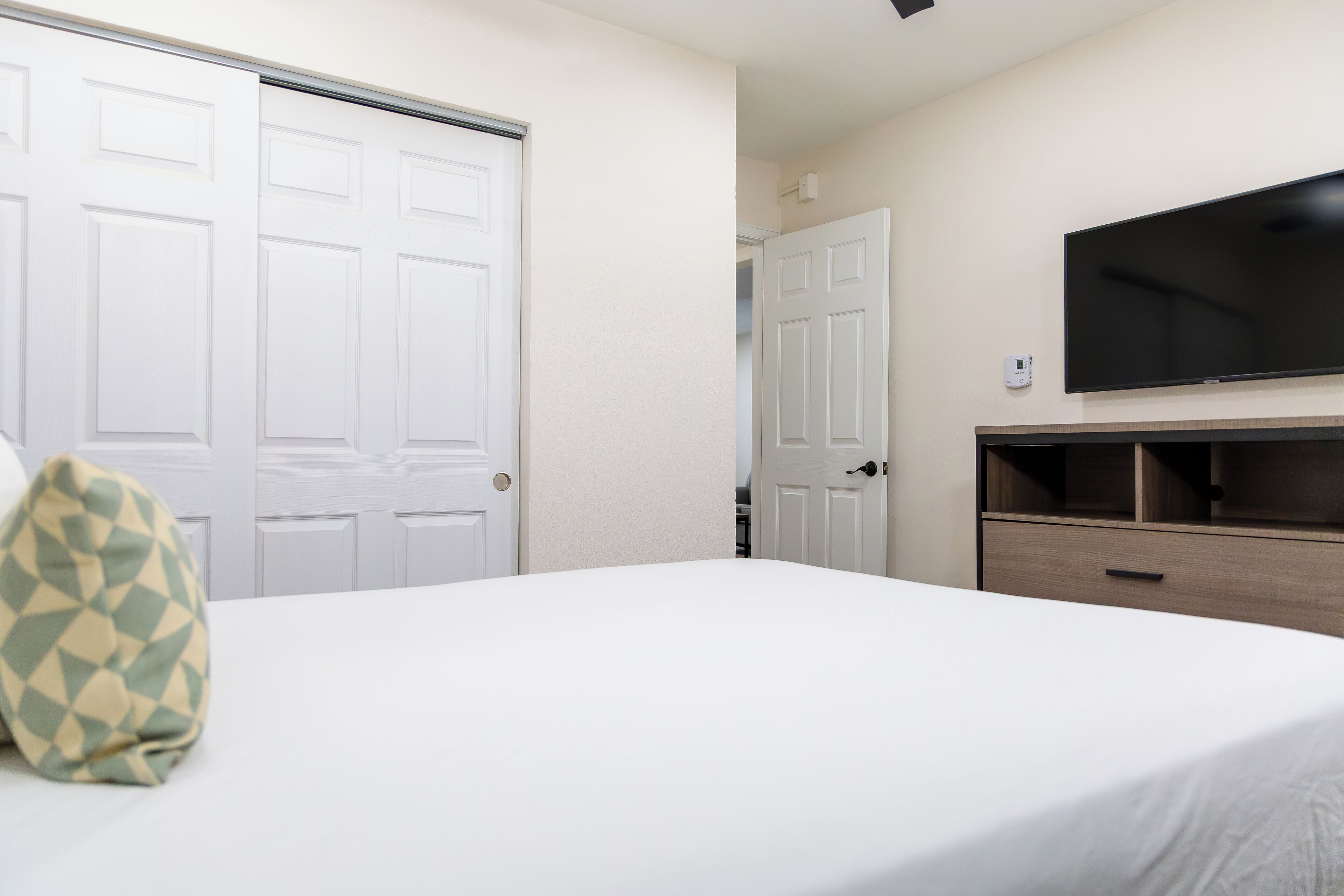 A hotel room with a bed, a TV mounted on the wall, and a door leading to a closet.