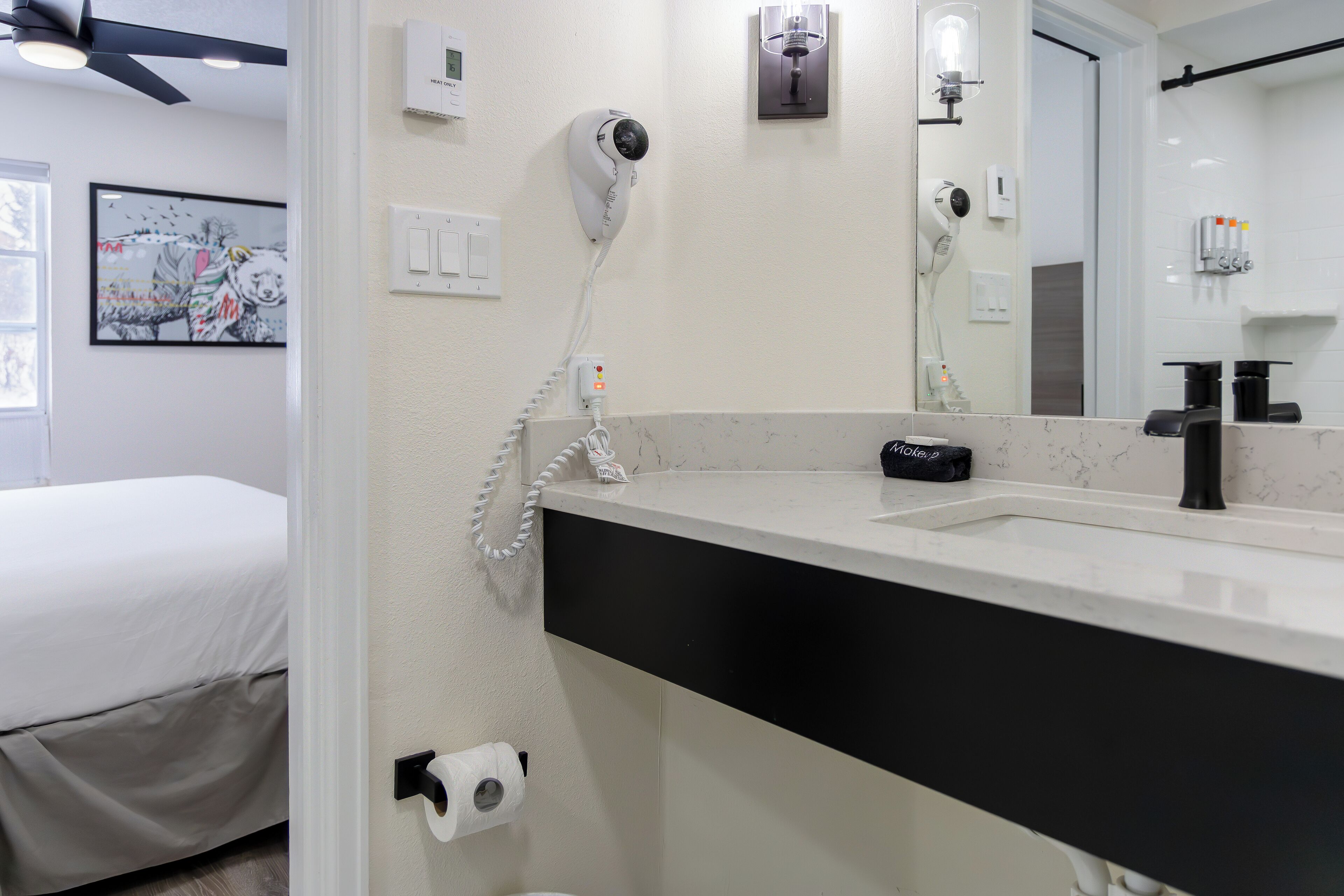A hotel bathroom with a white sink, black countertop, and a hairdryer mounted on the wall.