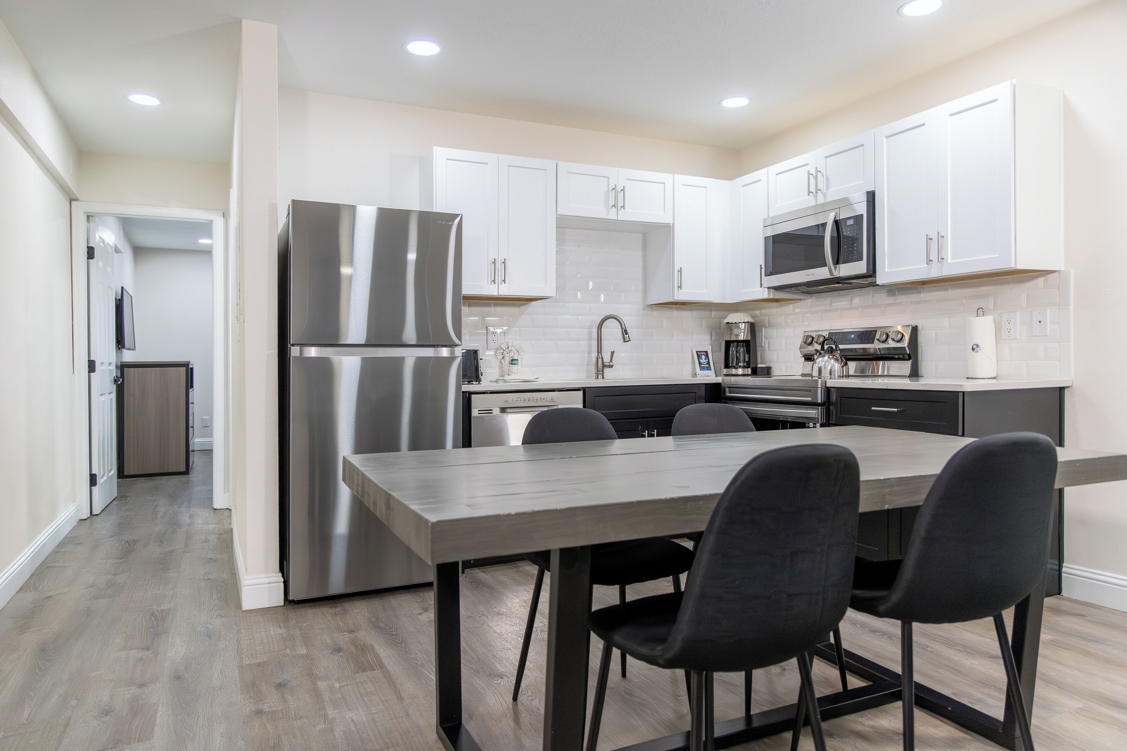 Una cocina moderna con armarios blancos, electrodomésticos de acero inoxidable y una mesa de comedor de madera con sillas.