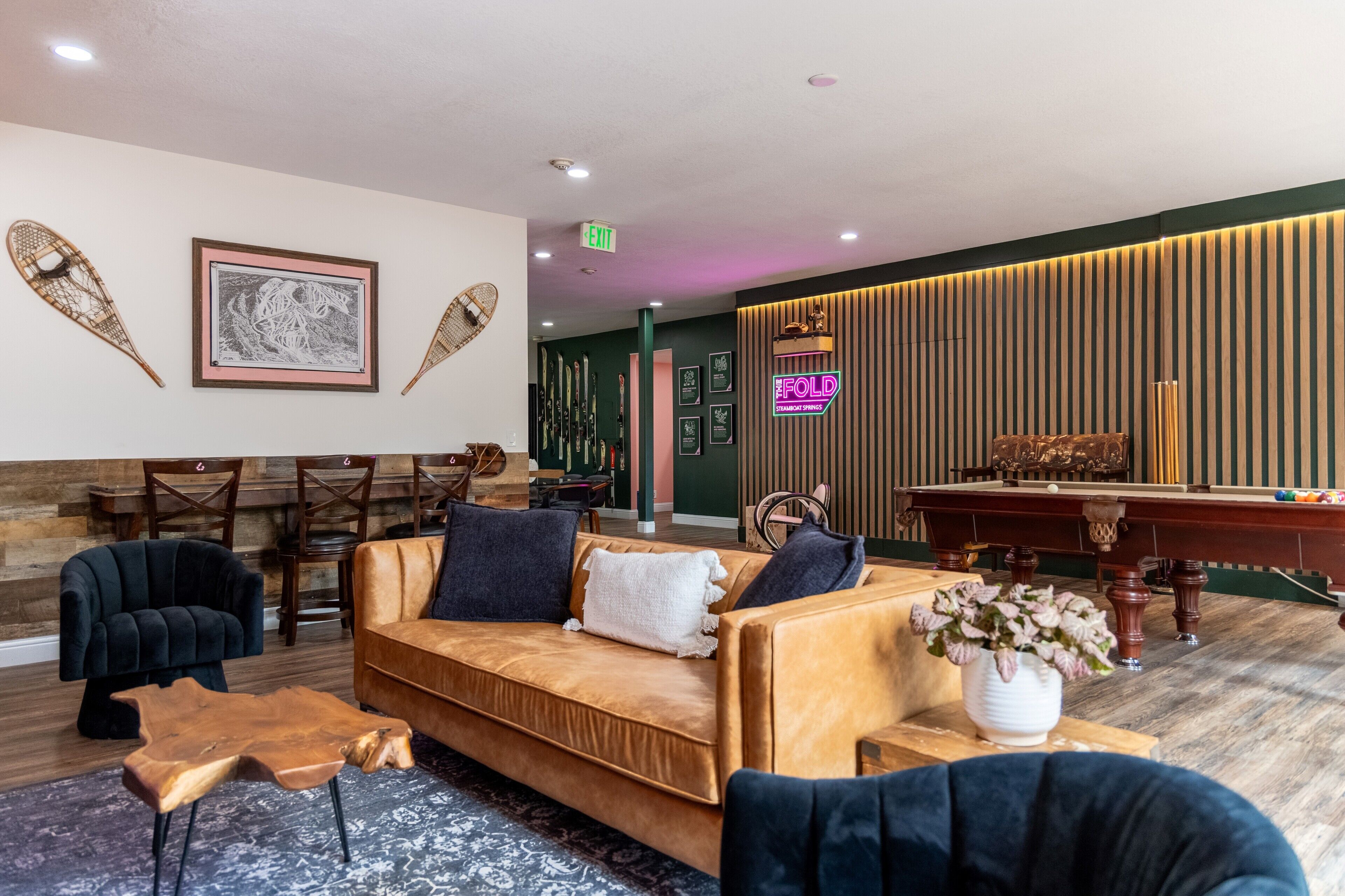 Un hall d'entrée avec un canapé, des fauteuils, une table de billard et un panneau lumineux au néon.