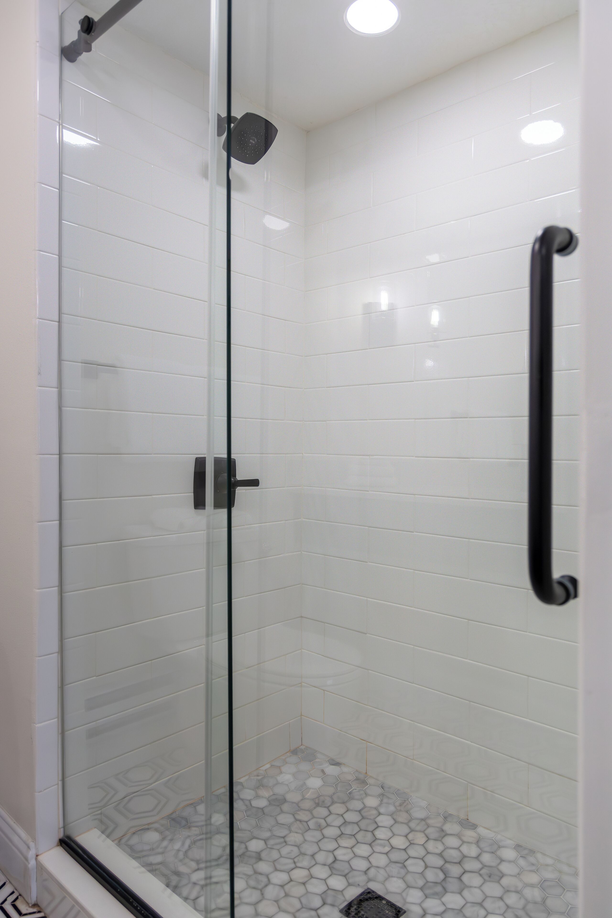 A glass-enclosed shower with white tiles and a hexagonal patterned floor.