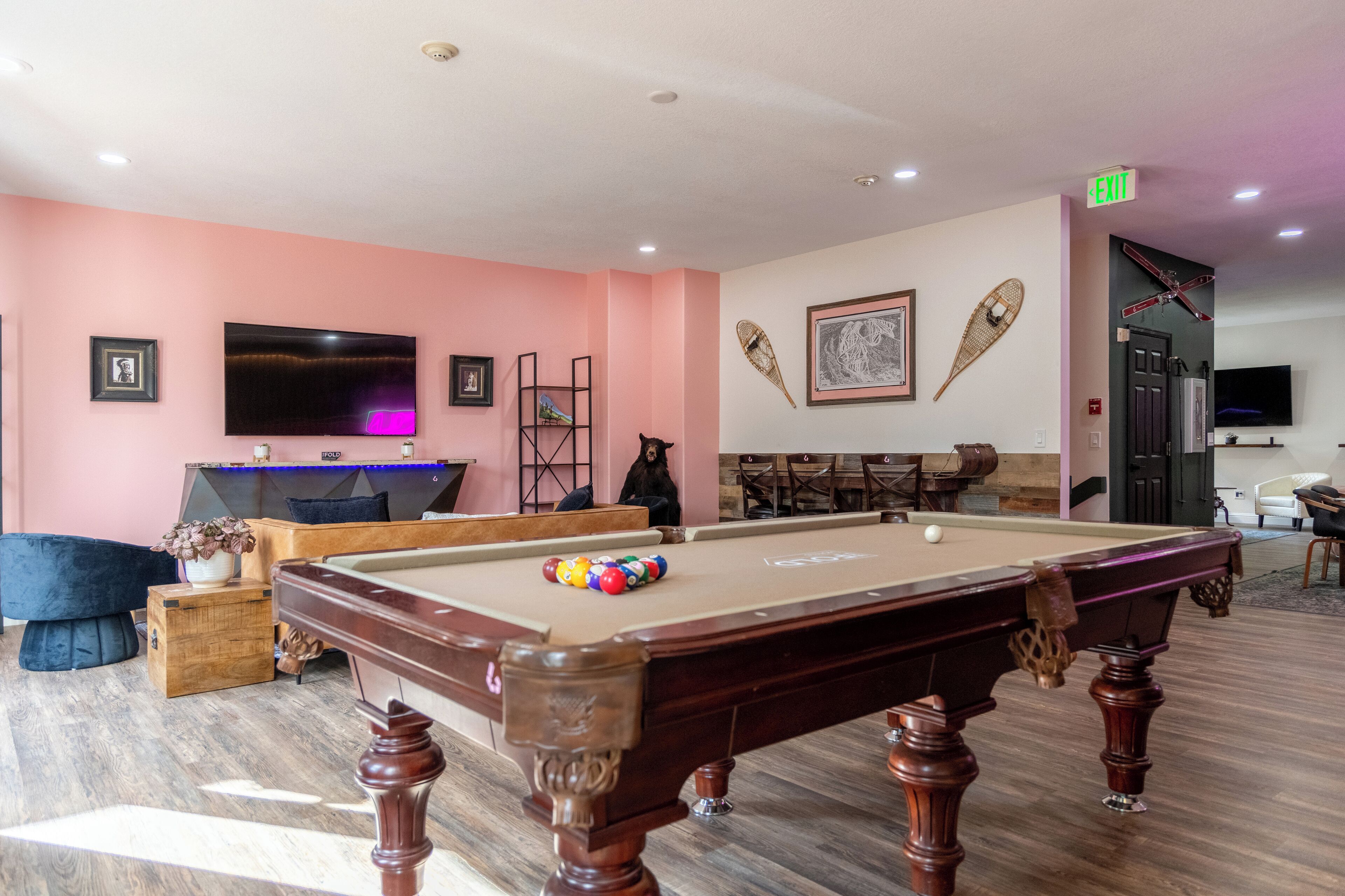 Una mesa de billar con bolas, un televisor y un soporte para billares en una habitación con paredes rosas y suelo de madera.
