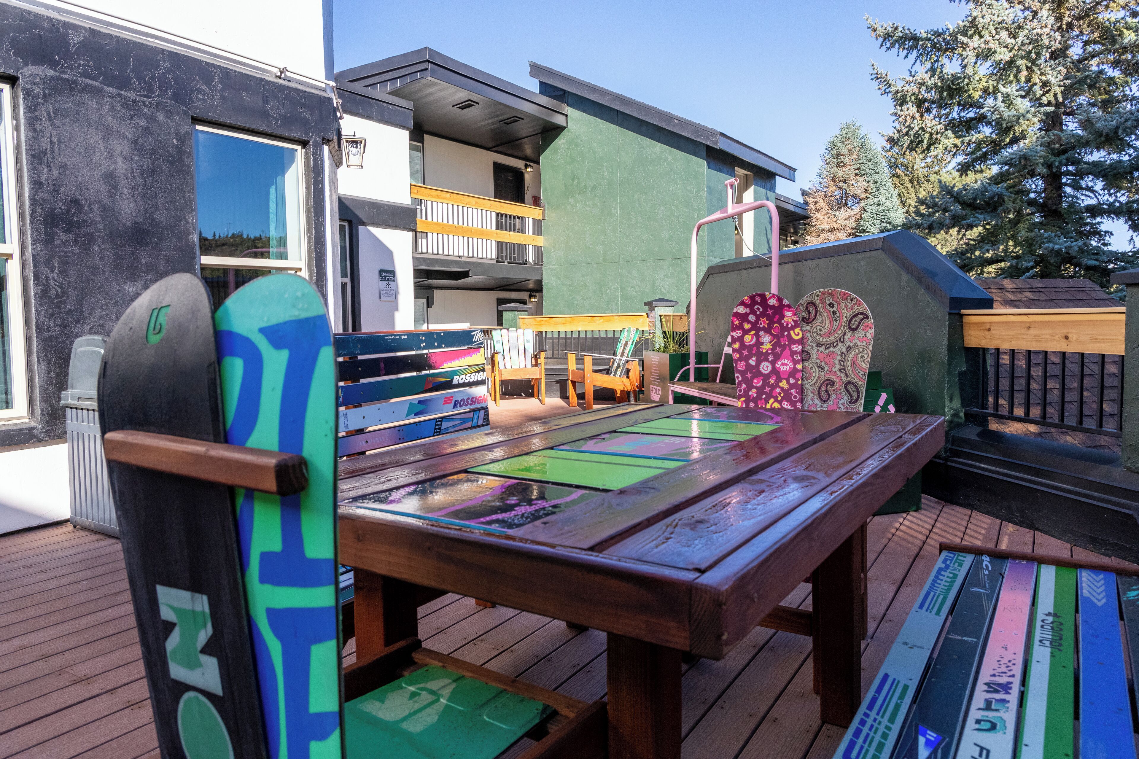 A wooden deck with colorful mats, a bench, and a table.