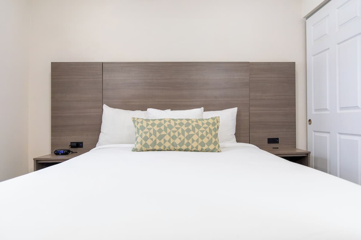 Een hotelkamer met een groot bed, een houten hoofdbord, twee nachtkastjes en een witte deur.