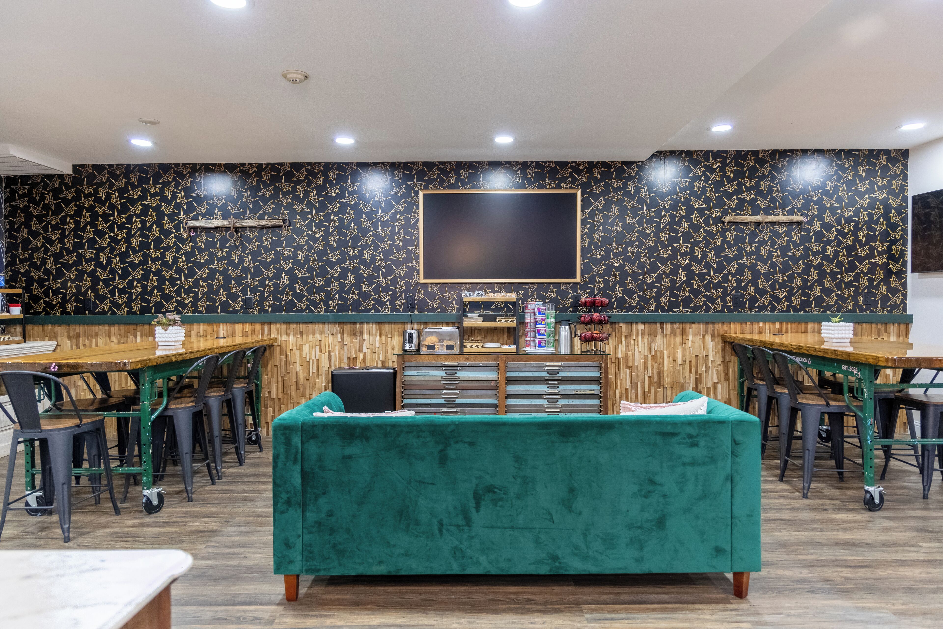 A modern restaurant with a black and gold patterned wall, a large flat-screen TV, and a green upholstered sofa.