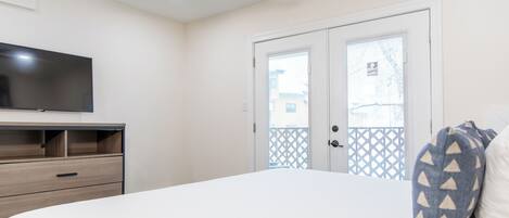 Un dormitorio con cama, televisor en un mueble bajo, ventilador de techo y puerta con vista al exterior.