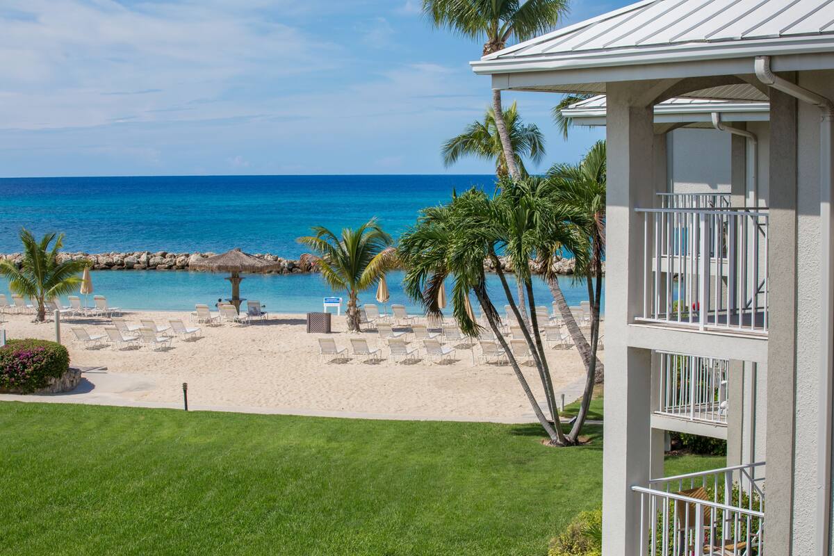 A beachfront hotel with a pool, palm trees, and beach chairs.
