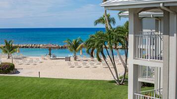 A beachfront hotel with a pool, palm trees, and beach chairs.