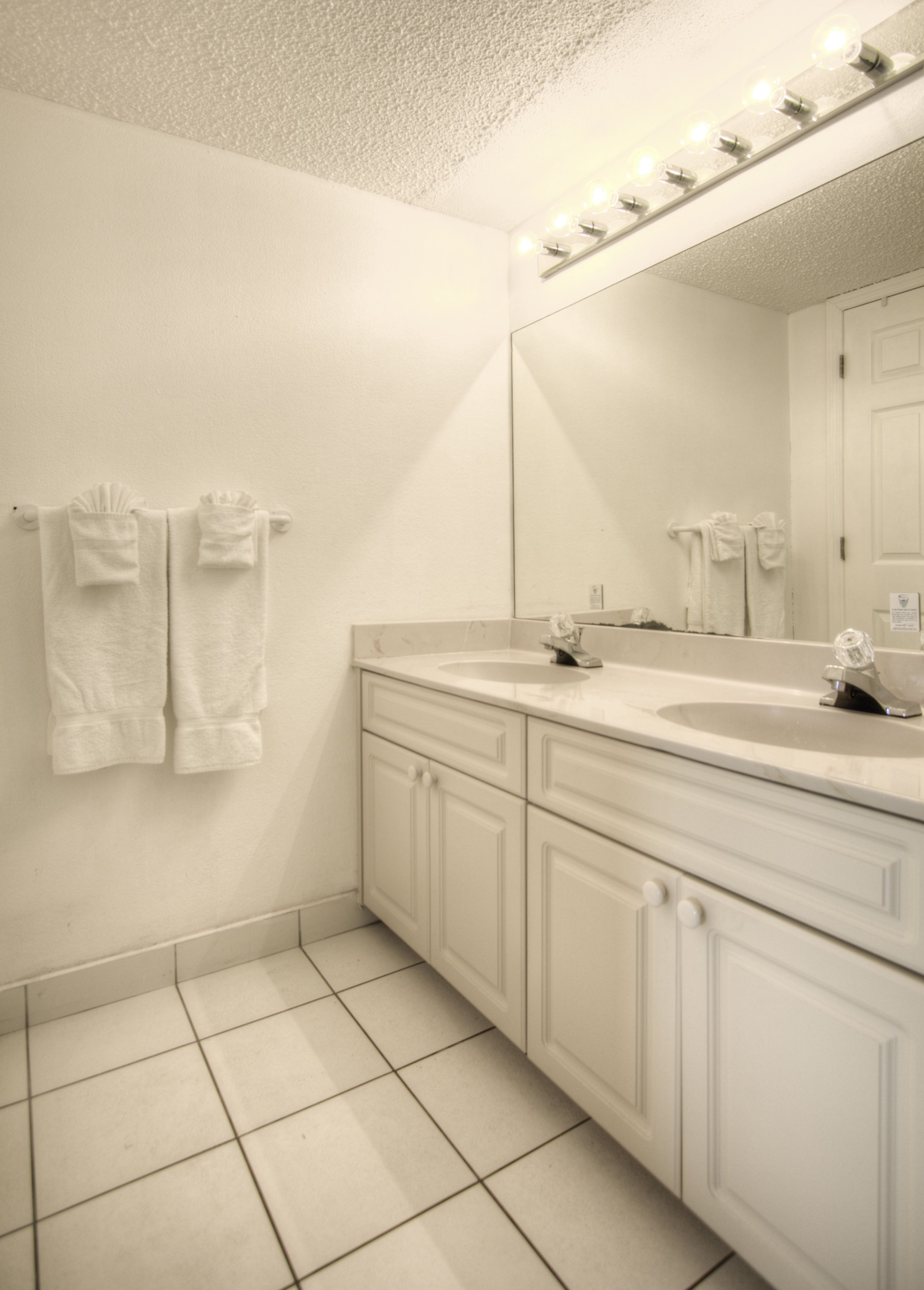 A bathroom with two sinks, a large mirror, and white towels hanging on the wall.