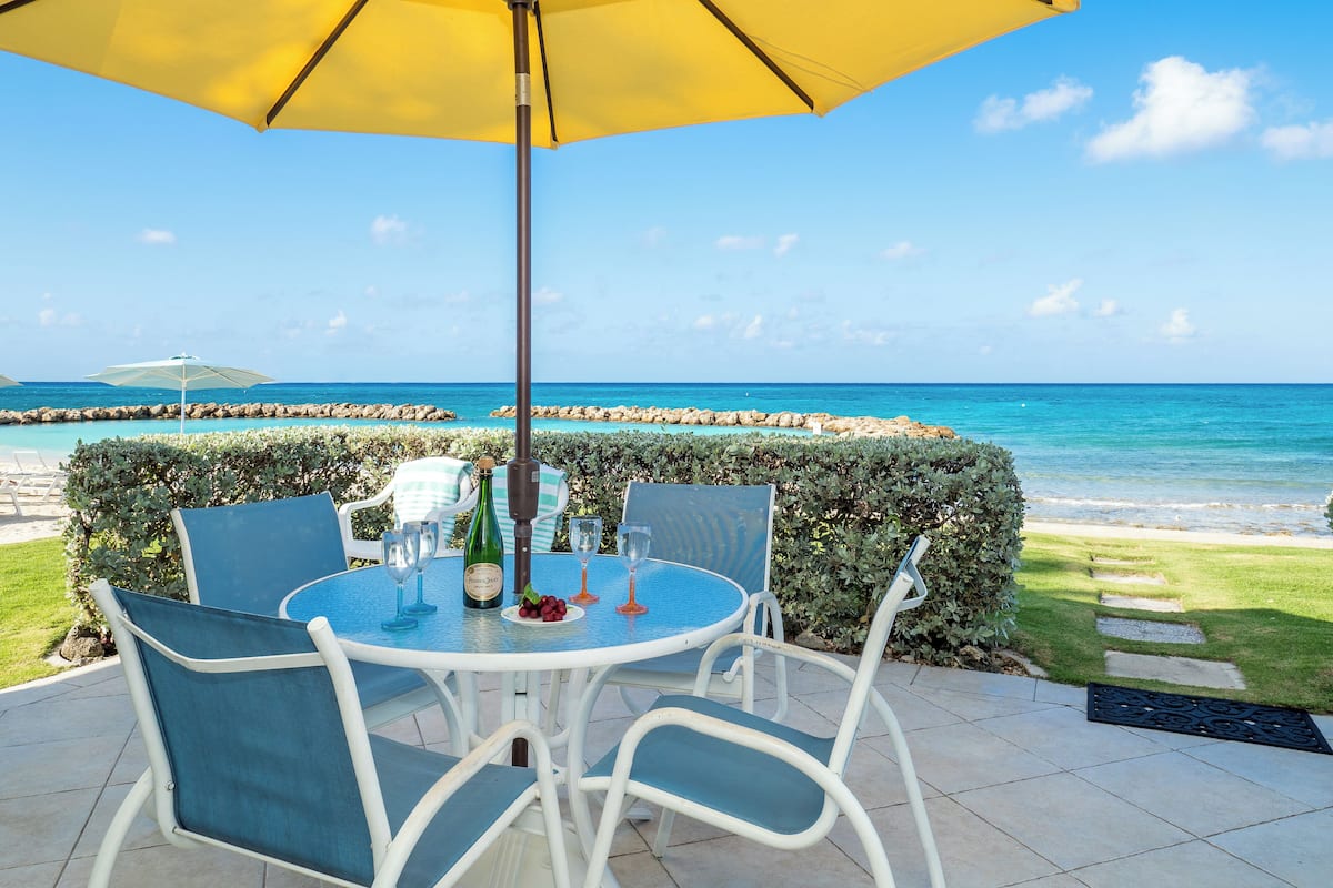 An outdoor patio with a table and chairs, a yellow umbrella, and a view of the ocean.