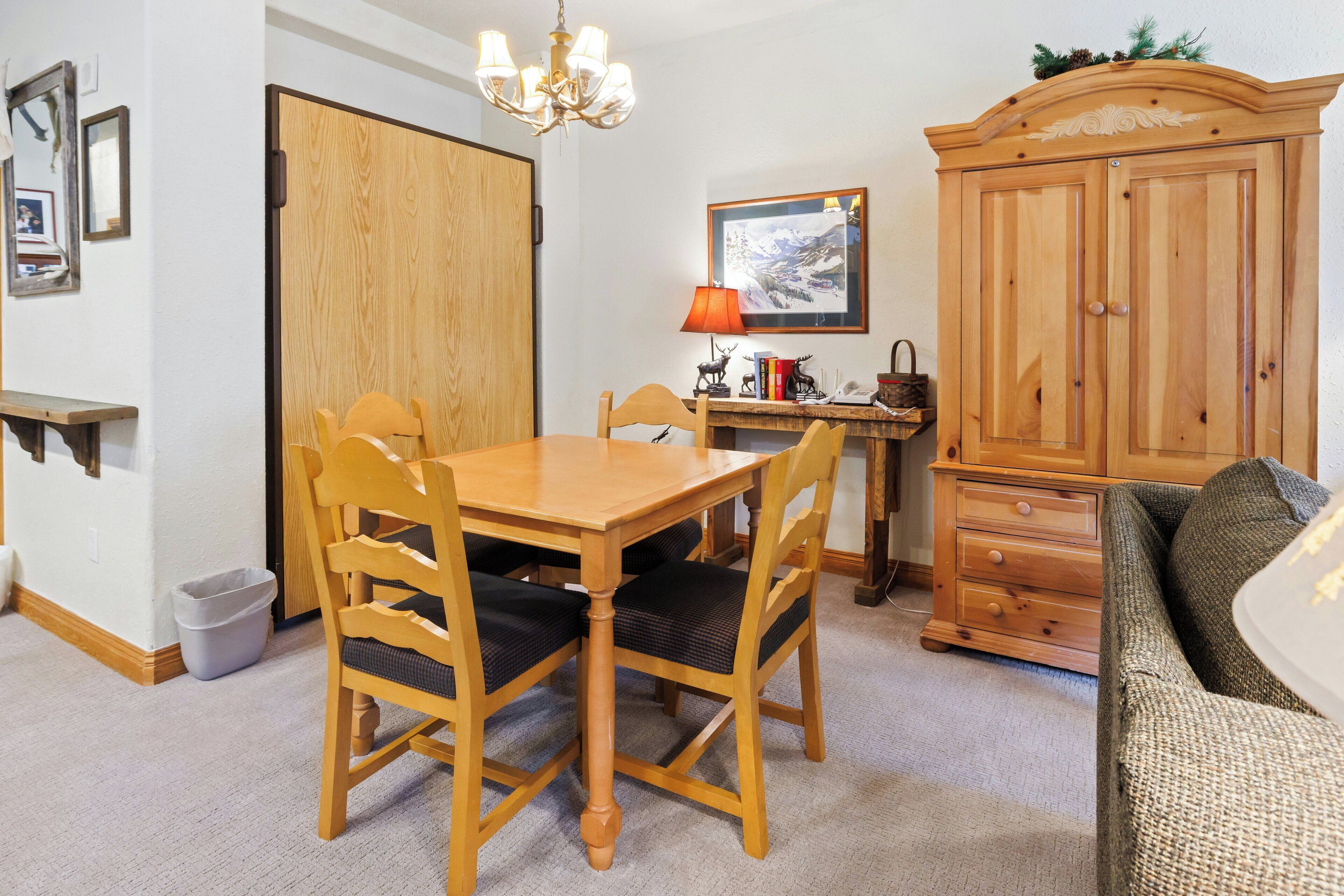 Un coin repas avec une table et des chaises en bois, une lampe, un tableau encadré au mur et un buffet en bois.