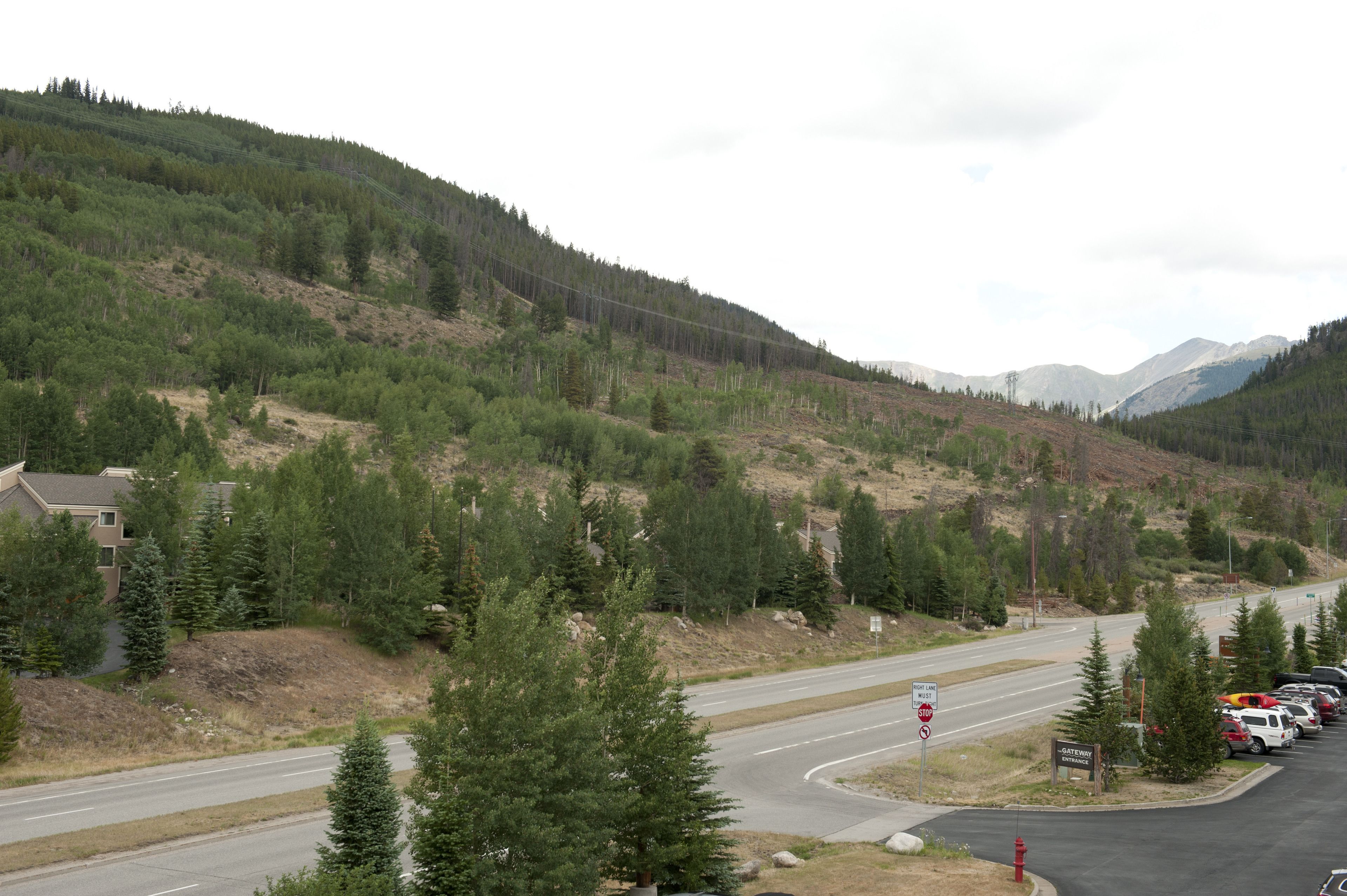 A road curving through a mountainous area with a parking lot and a building on the left.