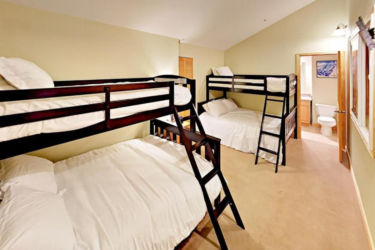 A room with bunk beds, a bathroom with a toilet and sink, and a door leading to another room.