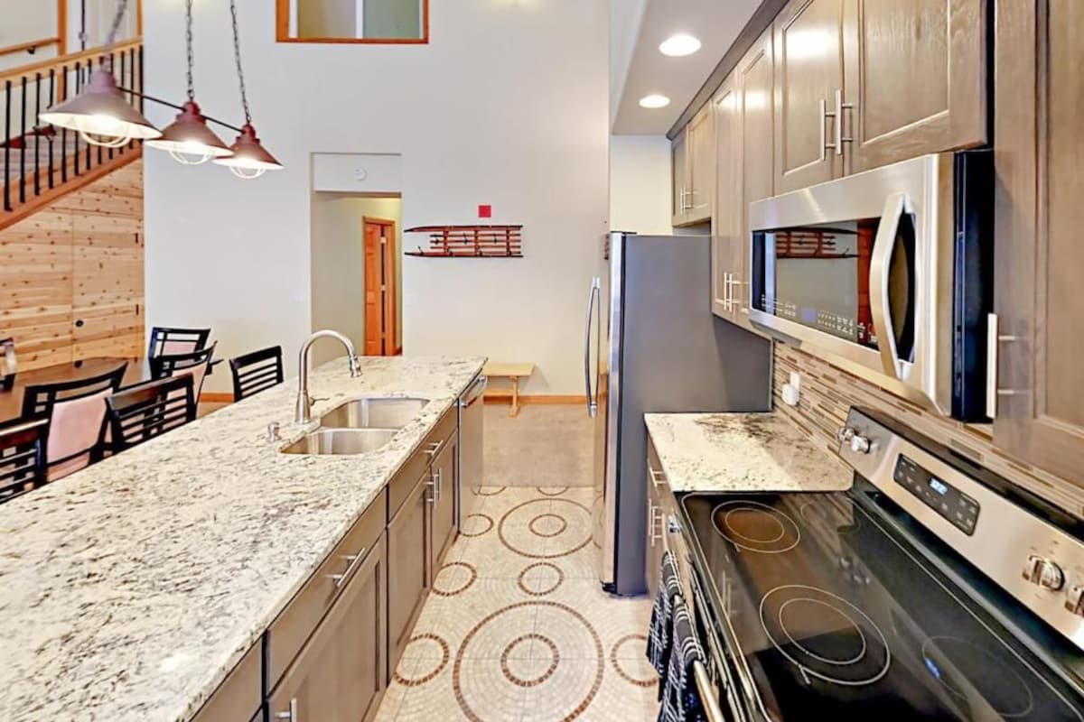 A modern kitchen with granite countertops, stainless steel appliances, and a wooden staircase.