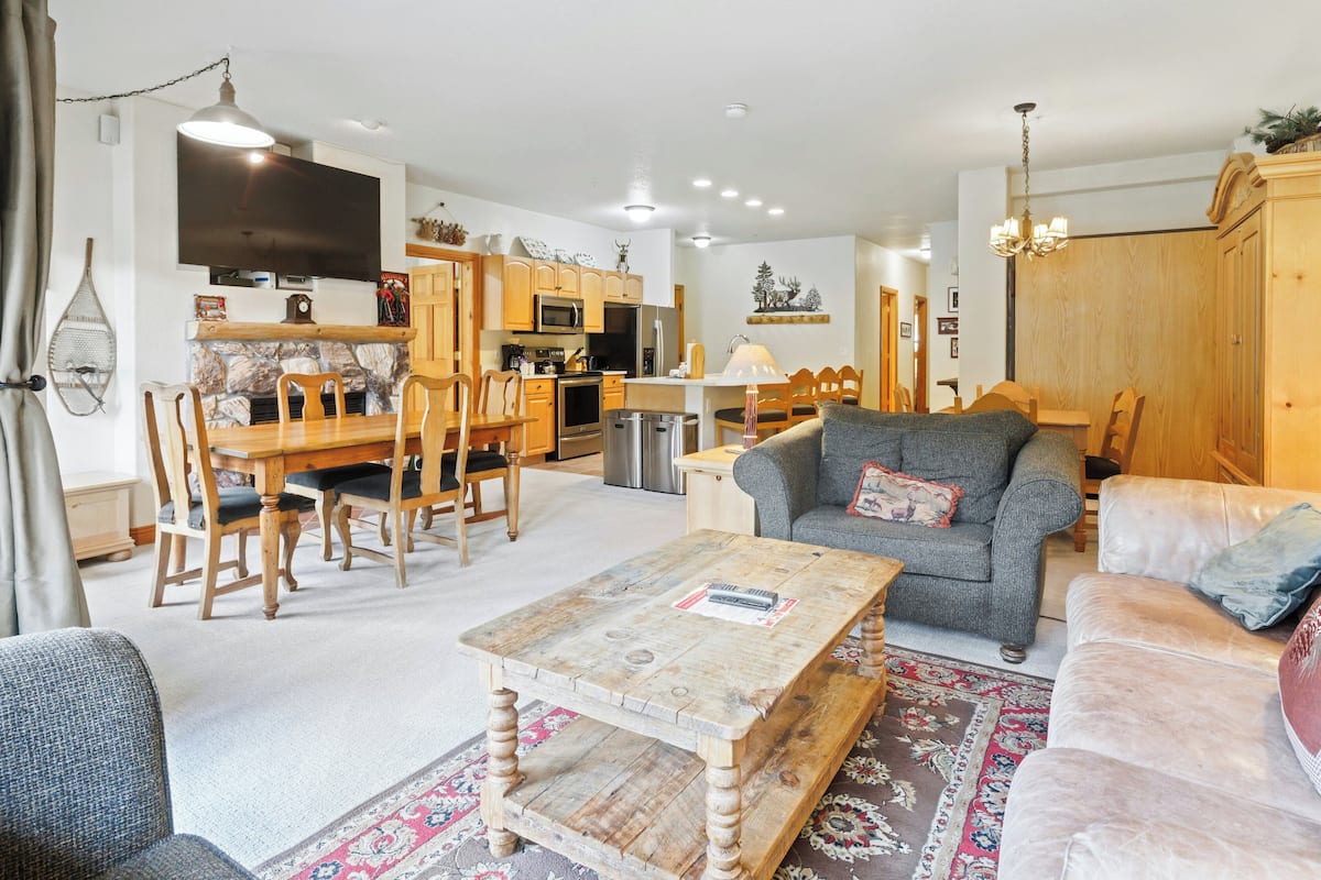 A spacious living room with a wooden coffee table, a grey sofa, and a dining area with wooden chairs and a table.